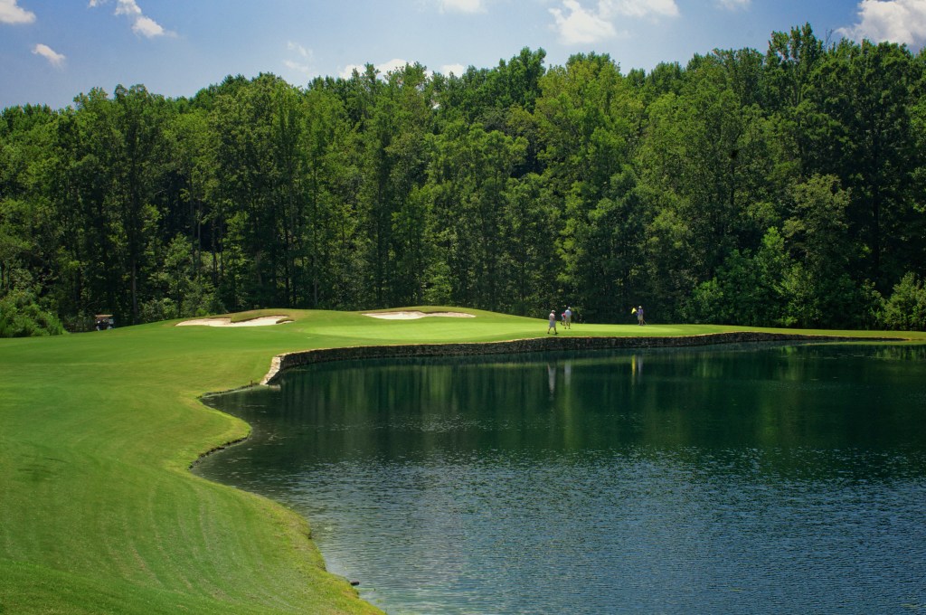 View of golf course with players on far edge of pond