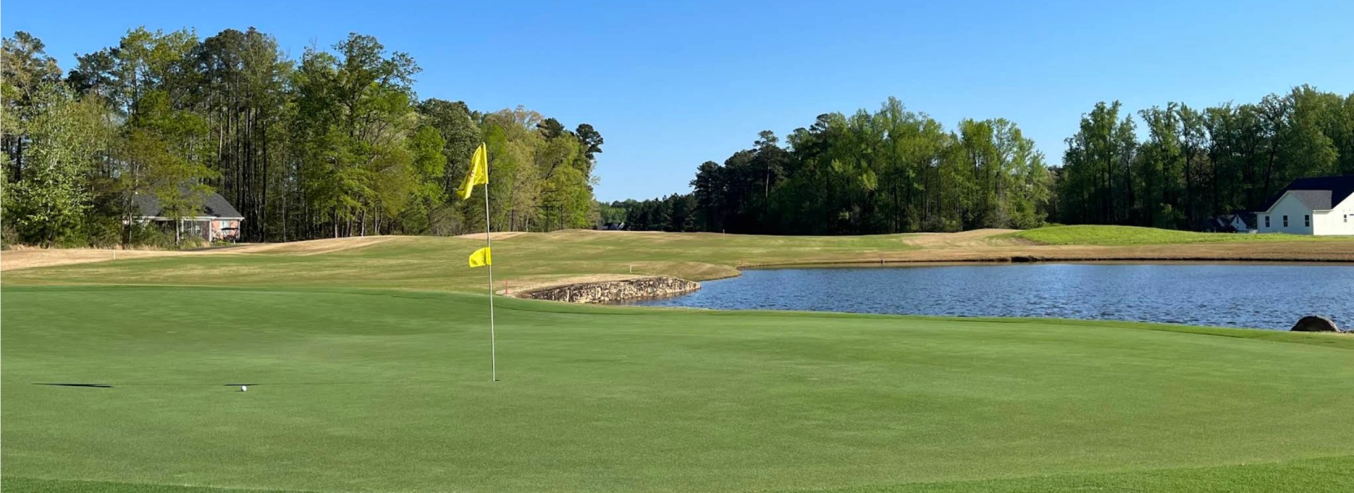 Green with a yellow flagstick beside a pond at Belmont Lake Golf Club